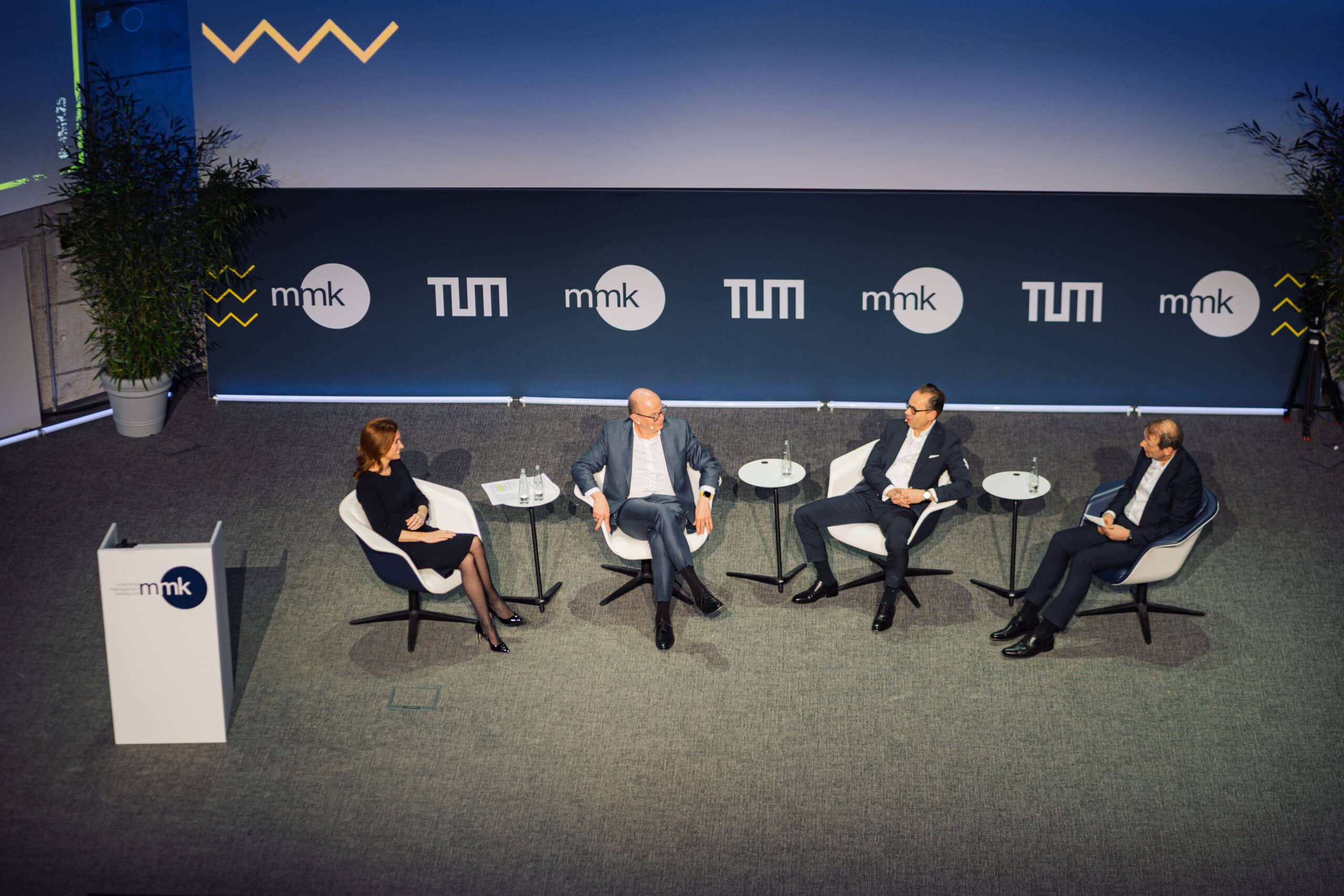 Discussion round with four people on a stage, in the background a banner with the words 