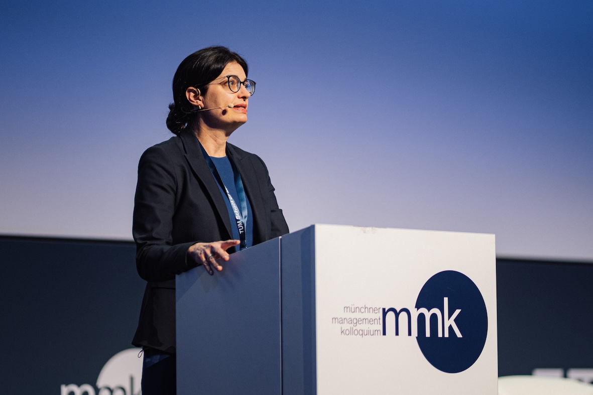 Eine Frau mit Brille steht an einem Rednerpult mit dem Logo 