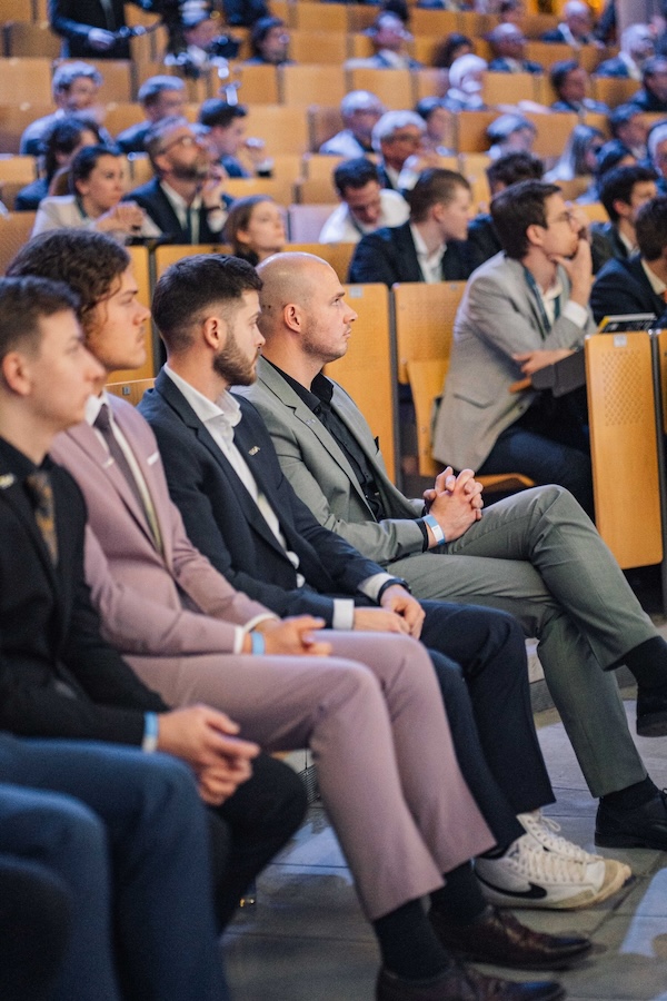 Eine Gruppe von Männern in Anzügen sitzt in einem Hörsaal und hört aufmerksam zu.