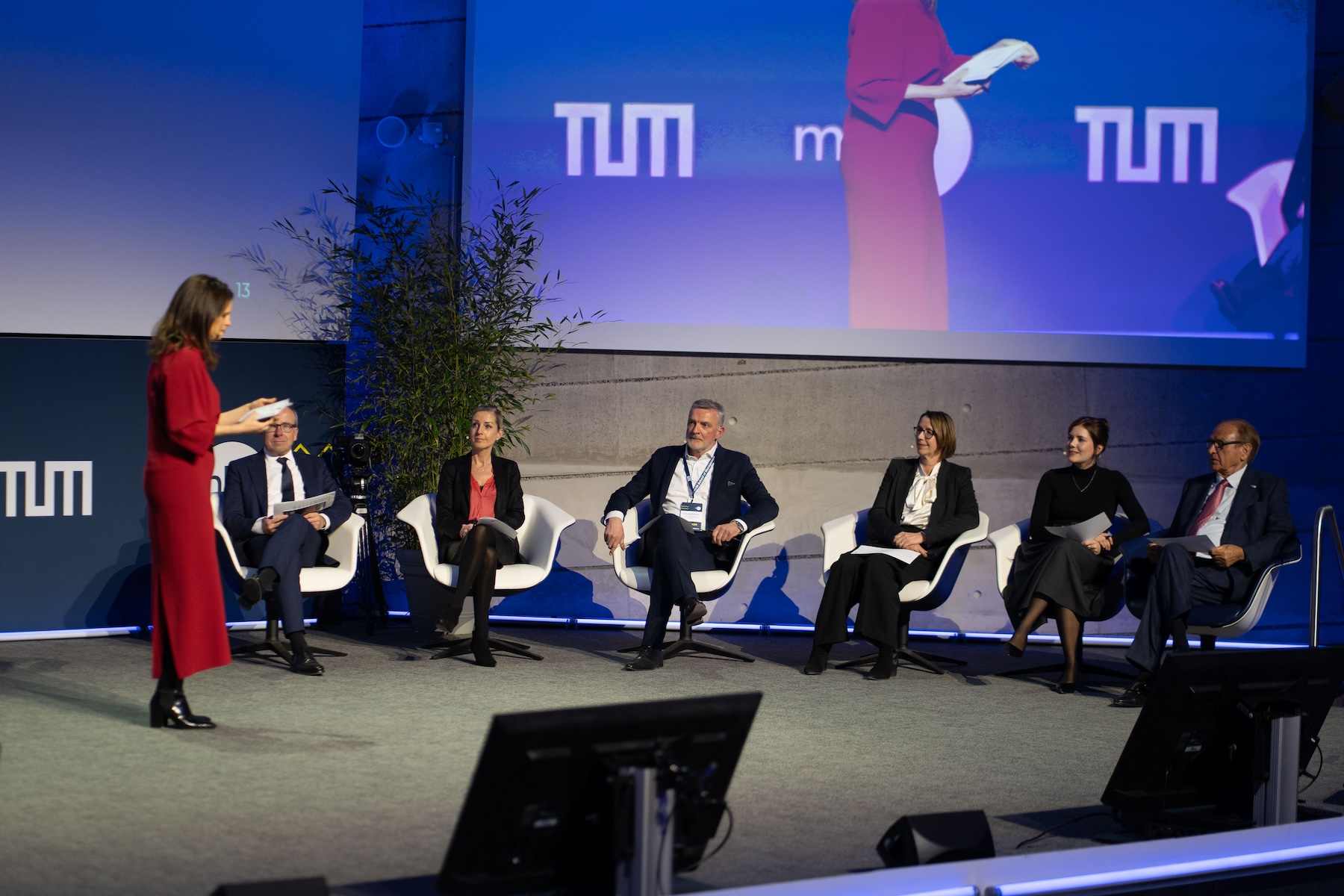 Paneldiskussion mit mehreren Personen auf der Bühne, im Hintergrund das Logo der Technischen Universität München (TUM).